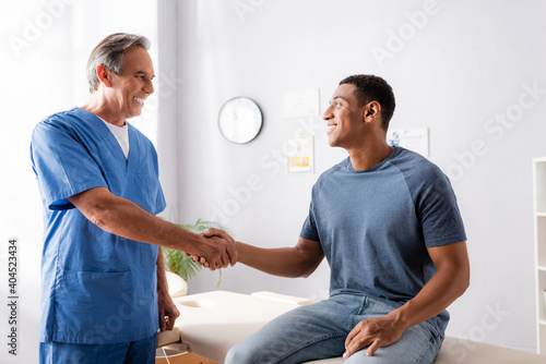 happy chiropractor shaking hands with african american patient photo
