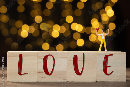 Miniature people man stand on wood cubic holding red heart for lover with yellow light bokeh background,Valentines concept