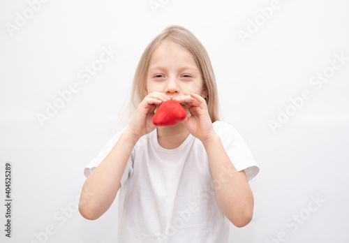 A little girl in a white T-shirt inflates a red heart-shaped balloon. Child preparing for the holiday valentine's day