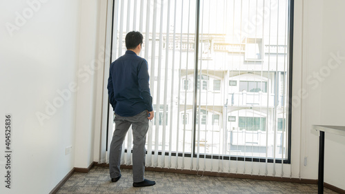 A young man in a blue shirt stood looking outside the building by the window.