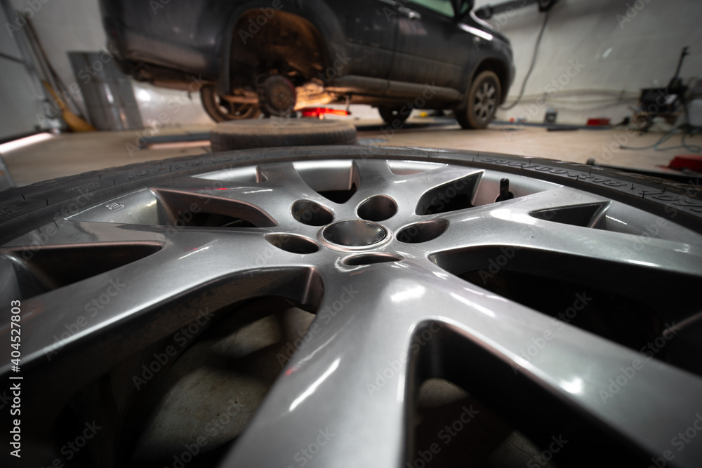 In the foreground is a wheel on the floor. In the background is a car. Service and maintenance concept. Planned and sudden. Replacement of brake pads. Selective focus In the foreground is a wheel on the floor. In the background is a car. Service and maintenance concept. Planned and sudden. Replacement of brake pads. Selective focus