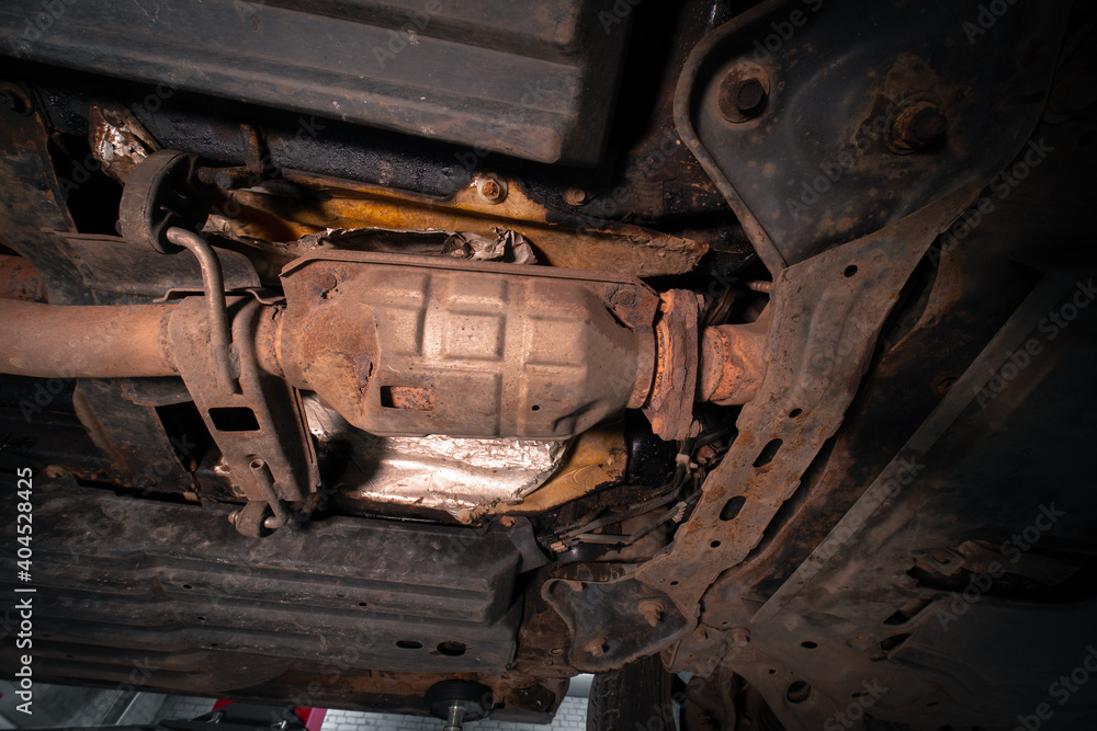 Close-up on the part of the bottom of the car from the front of the exhaust pipe and the catalyst disassembled during the repair in the workshop auto service vehicles Close-up on the part of the bottom of the car from the front of the exhaust pipe and the catalyst disassembled during the repair in the workshop auto service vehicles