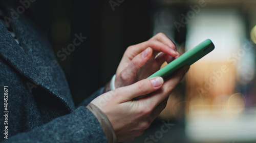 Side view of young woman   s hands holding smartphone in green case and typing on it. Present-day technologies and mobile digital devices make communication and interaction between individuals easier