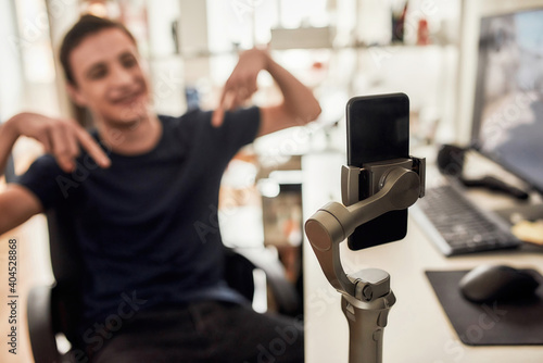 Teenage guy using smartphone while playing game and recording video. Blogging, technology concept. Focus on mobile phone on a tripod photo