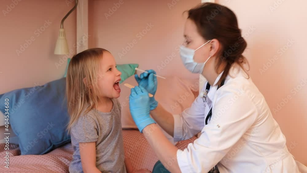 Pediatrician taking saliva test sample from elementary age girl's mouth performing Saliva testing (Salivaomics) diagnostic procedure at home during coronavirus COVID-19 quarantine Pediatrician taking saliva test sample from elementary age girl's mouth performing Saliva testing (Salivaomics) diagnostic procedure at home during coronavirus COVID-19 quarantine