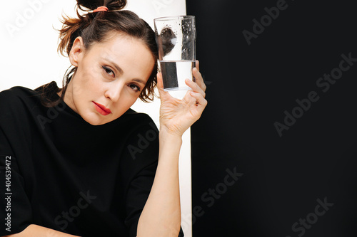 Beauty portrait of a girl in a black dress with a glass of water on a black and white background. 