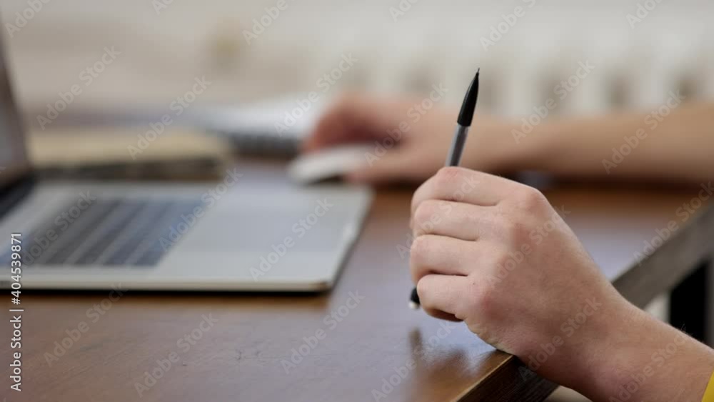 Close up of male hands working at a laptop. In one hand, the guy turns a pen. The concept of working with information. Close up of male hands working at a laptop. In one hand, the guy turns a pen. The concept of working with information.