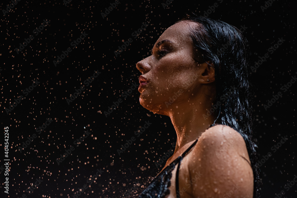 sensual, wet woman posing under rain on dark background