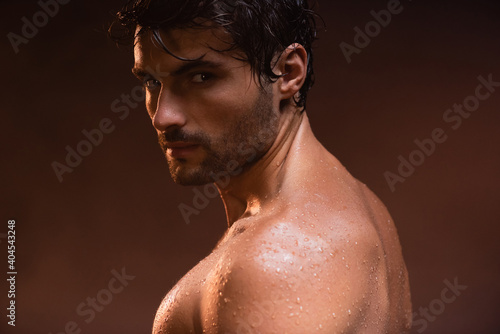 wet, sexy man looking at camera while posing on dark background