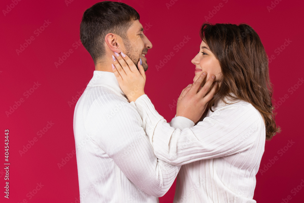 A young family couple look at each other with loving eyes, touching tenderly their faces. Red background. A young family couple look at each other with loving eyes, touching tenderly their faces. Red background.