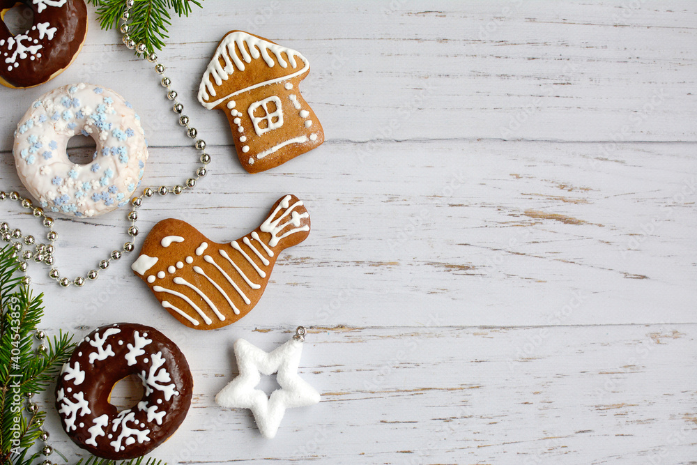 Christmas cookies in the shape of a house and a bird, donuts in chocolate glaze, New Year's decor on a light wooden background with side space for text. Layout