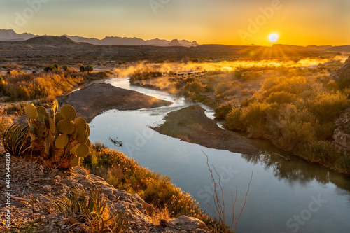 Canvas Print A prickly pear cactus and the sun rising over distance mountains and a river mea