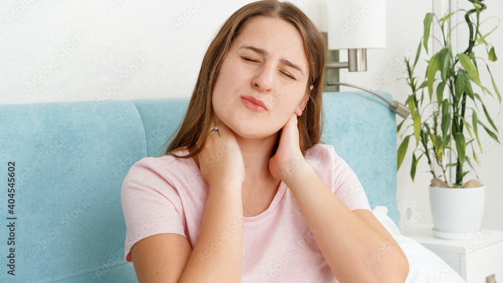 Portrait of young woman suffering from pain in neck massaging aching muscles Portrait of young woman suffering from pain in neck massaging aching muscles