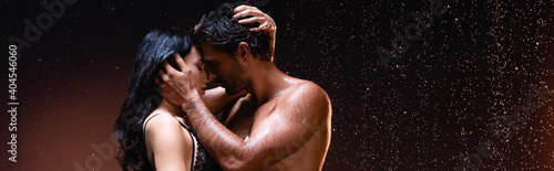 side view of couple embracing and kissing under rain on dark background, banner