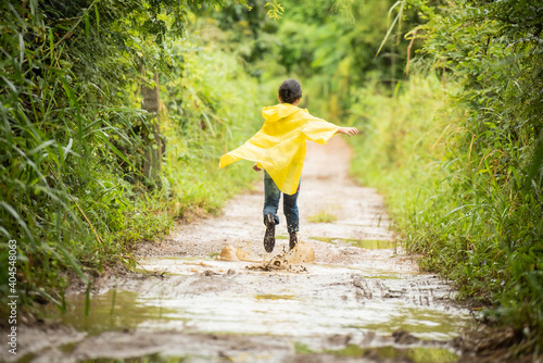 happy little asian  girl running and jumping in puddles after rain in summer. child play in autumn rain. kid playing on the nature outdoors. girl is wearing yellow raincoat and enjoying rainfall..