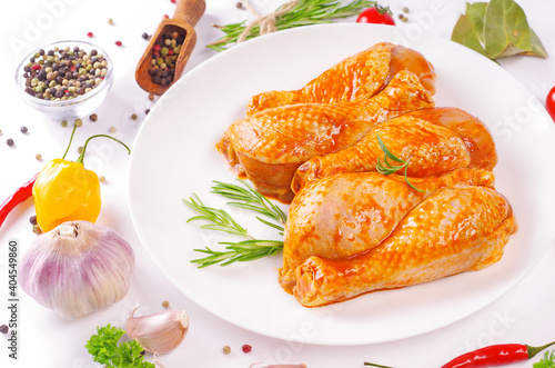 Raw chicken legs with herbs and spices on white background.Marinated chicken dramstick on a white plate with spices for cooking. photo