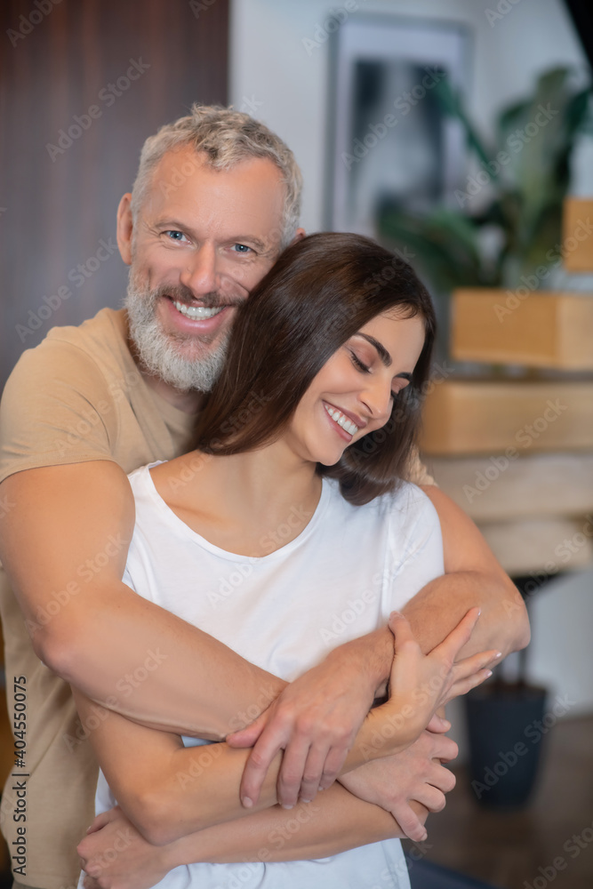 Bearded man and young woman hugging and looking happy Bearded man and young woman hugging and looking happy