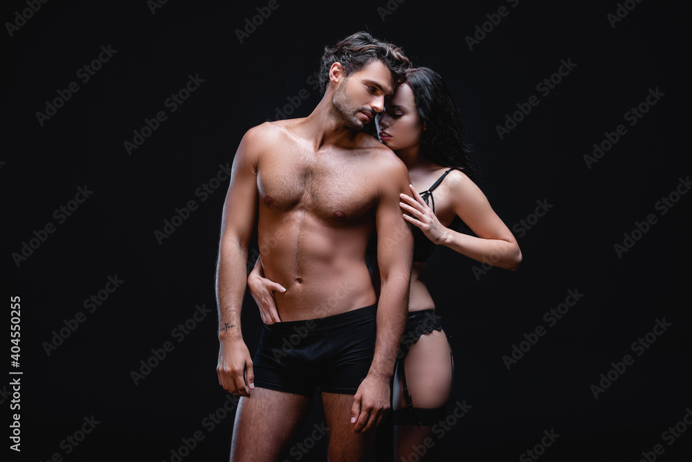 seductive woman in lace lingerie and stockings embracing sexy muscular man isolated on black