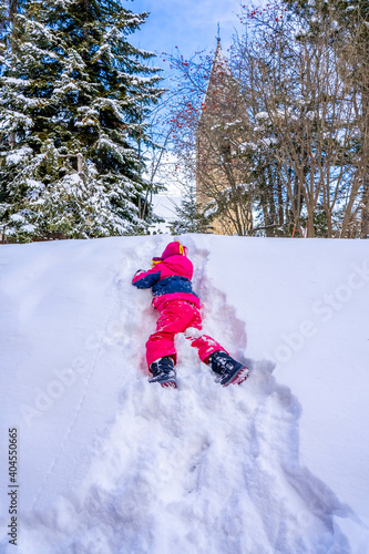 Funny little girl in colorful winter suit climbs the snow hill. Kids play and jump in snowy forest. Child playing with snow in winter. High quality photo