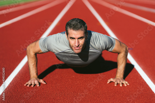 Mature fitness man looking and doing push-ups on the red running track. Copy space. Close up. Lifestyle and sports