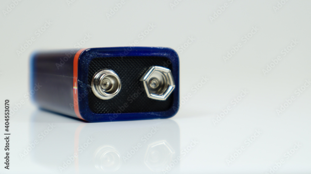 One blue used PP3 battery on a white background with reflection. Main battery for personal power supplies. Close-up of a scratched and used battery connector. One blue used PP3 battery on a white background with reflection. Main battery for personal power supplies. Close-up of a scratched and used battery connector.