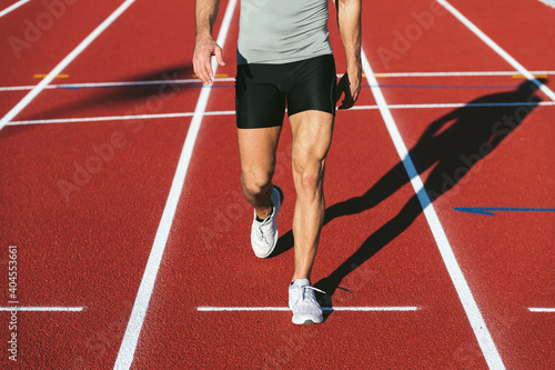 close-up shot of athletic man legs walking in black shorts on red running track in summer. Lifestyle and sports