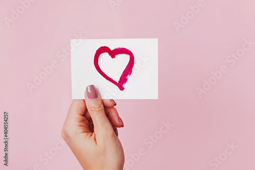 Woman's hand holding a paper card with heart symbol drawn on it photo