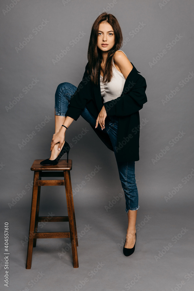 Amazing brunette with long hair in jacket and jeans put her foot on the back of a chair Amazing brunette with long hair in jacket and jeans put her foot on the back of a chair
