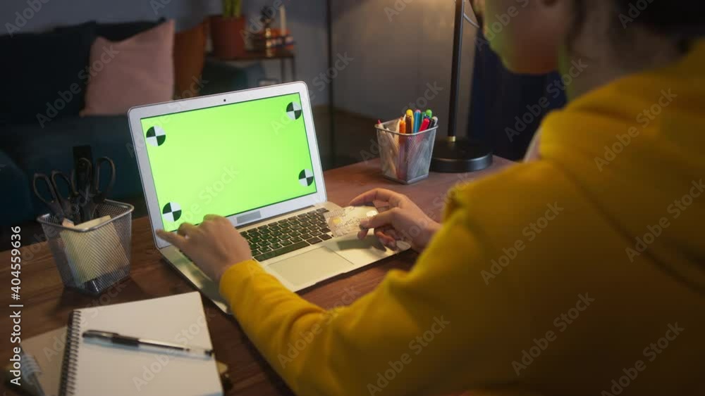 Beautiful Black Woman Sitting at Her Desk Works on a Laptop with Green chroma key Mock-up Screen. Late at Night in Her Living Room female Using Notebook Computer. Beautiful Black Woman Sitting at Her Desk Works on a Laptop with Green chroma key Mock-up Screen. Late at Night in Her Living Room female Using Notebook Computer.