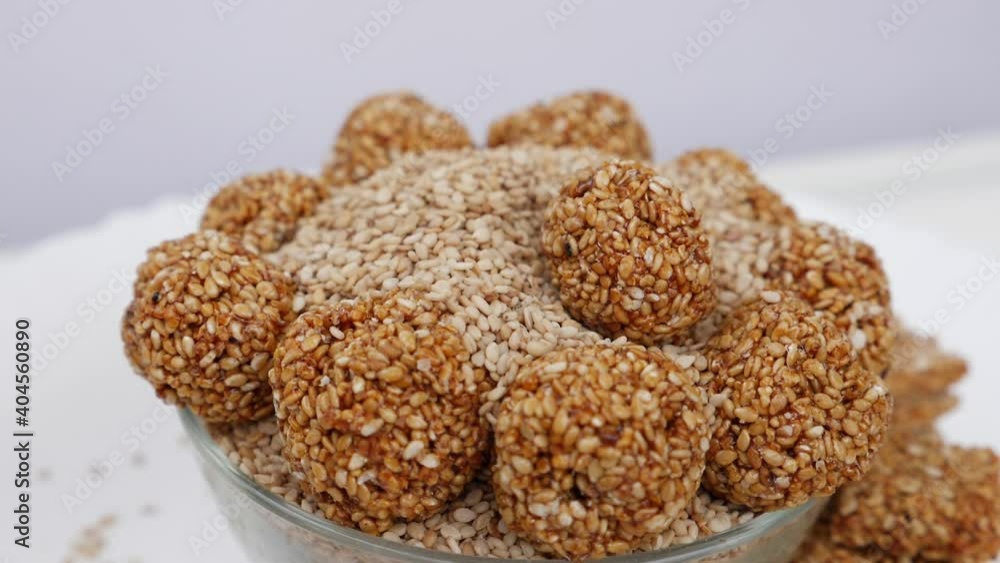 View of dropping sesame ladoo over bowl filled with sesame seeds View of dropping sesame ladoo over bowl filled with sesame seeds