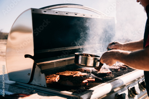Closeup of a man marinating beef steaks on a steel gas grill