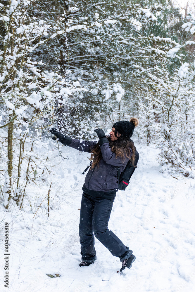 Young girl moving away from the snow on the branches of the trees in the forest. Snow falling from the branches of the trees