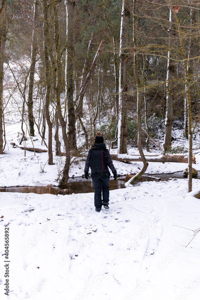 A person walking in the snow-covered forest and the source of a river.