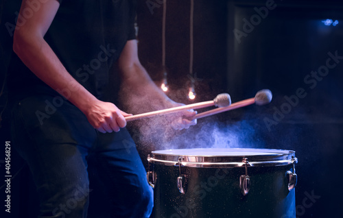 The drummer plays with mallets on floor tom in dark room.