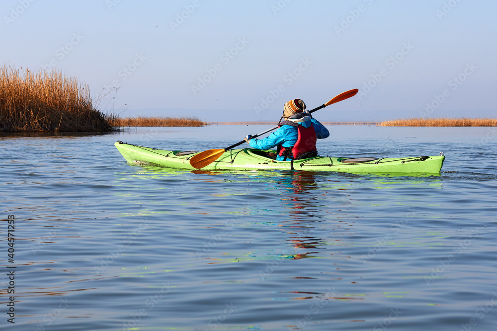 Man in a green kayak paddle at the lake in autumn season