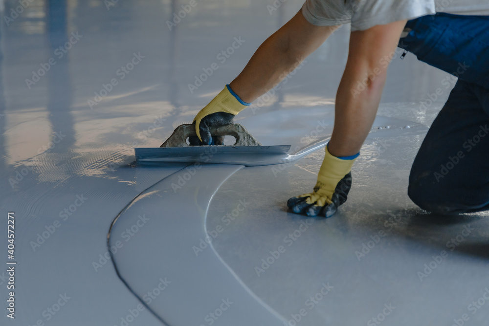 Ταπετσαρία The worker applies gray epoxy resin to the new floor