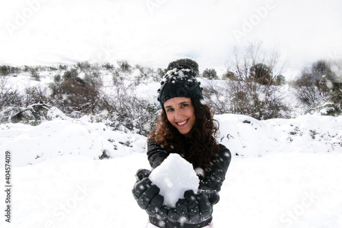 Girl in a black t-shirt and hat holding a snowball and smiling at the camera.