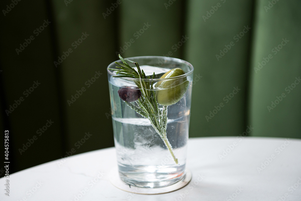 Clear cocktail garnished with rosemary and olives Clear cocktail garnished with rosemary and olives
