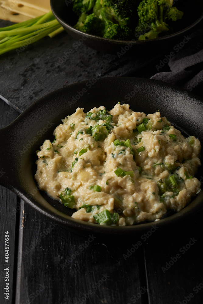 Scrambled eggs with broccoli and green onion served in dark plate with bread on table Scrambled eggs with broccoli and green onion served in dark plate with bread on table