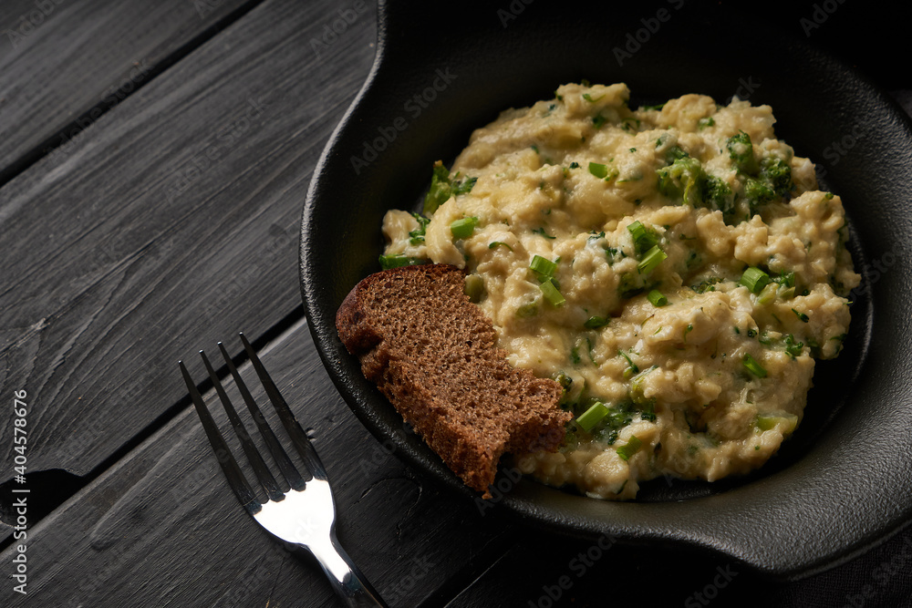 Scrambled eggs with broccoli and green onion served in dark plate with bread on table Scrambled eggs with broccoli and green onion served in dark plate with bread on table