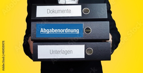 Abgabenordnung. Anwalt trägt einen Stapel Ordner. 3 Aktenordner mit Text-Beschriftung. Hintergrund gelb. photo