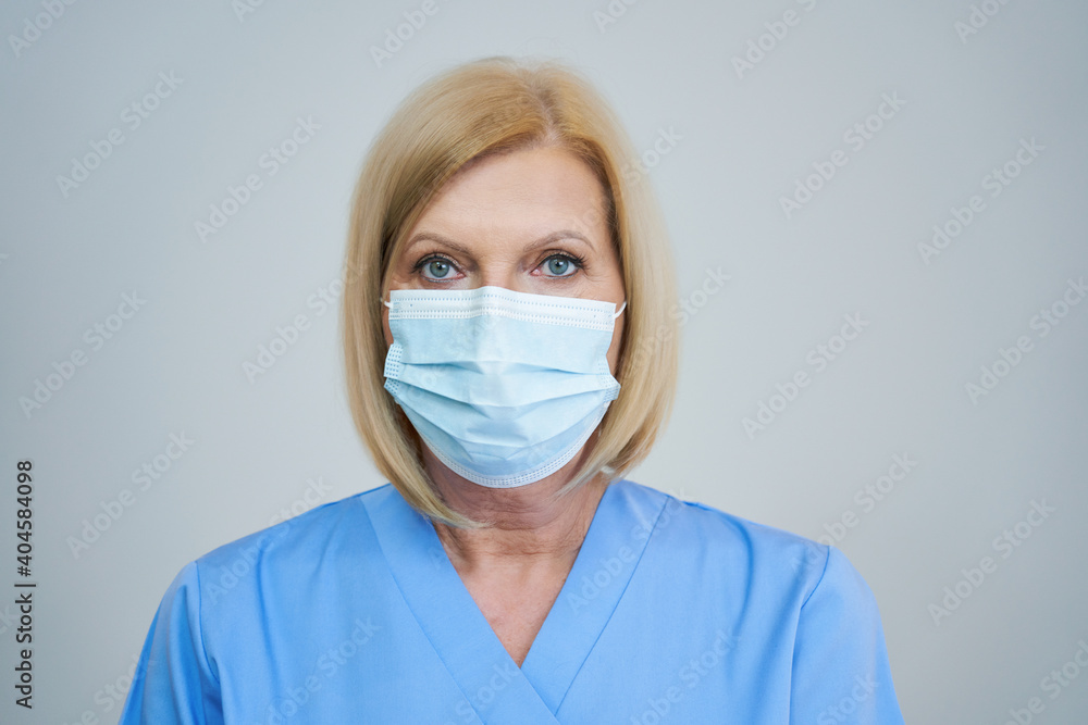 Senior female doctor posing in mask over gray background Senior female doctor posing in mask over gray background