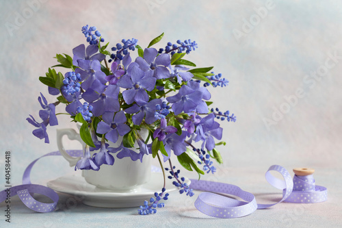 A bouquet of blue flowers of periwinkle, muscari and violets in a cup on a decorative background. Color of the year 2022.