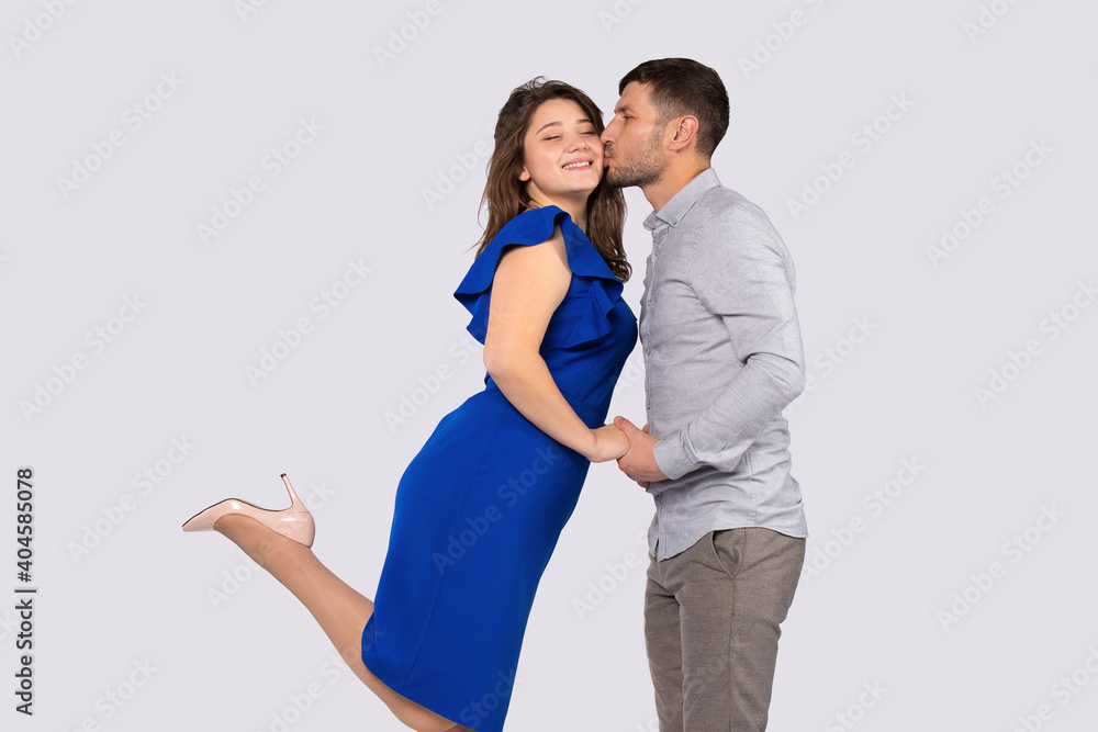 Fototapeta premium A man kisses his happy elegant woman, holding hands isolated over white background with side space.
