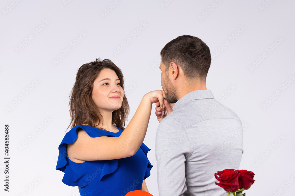 A man kisses girl's hand holding a bouquet of red roses behind his back on gray background. Valentine's day concept. A man kisses girl's hand holding a bouquet of red roses behind his back on gray background. Valentine's day concept.