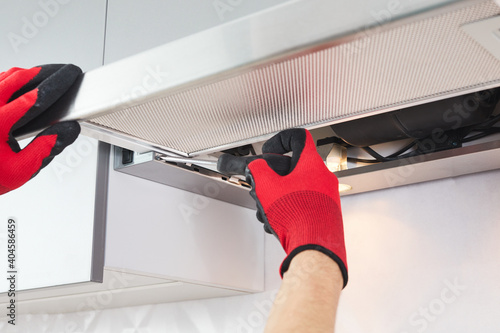 Male hands of an electrician troubleshoot a range hood. Cooker hood repair. Worker assemblying home range hood in kitchen furniture.