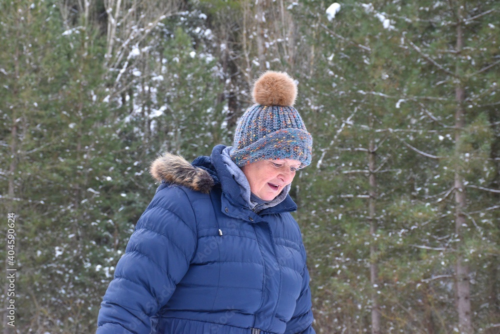 Retired woman in jacket and hat with colorful colors looking walking into a pine forest covered by snow. Scene after the snowstorm called Filomena in Spain. January 2021. Retired woman in jacket and hat with colorful colors looking walking into a pine forest covered by snow. Scene after the snowstorm called Filomena in Spain. January 2021.