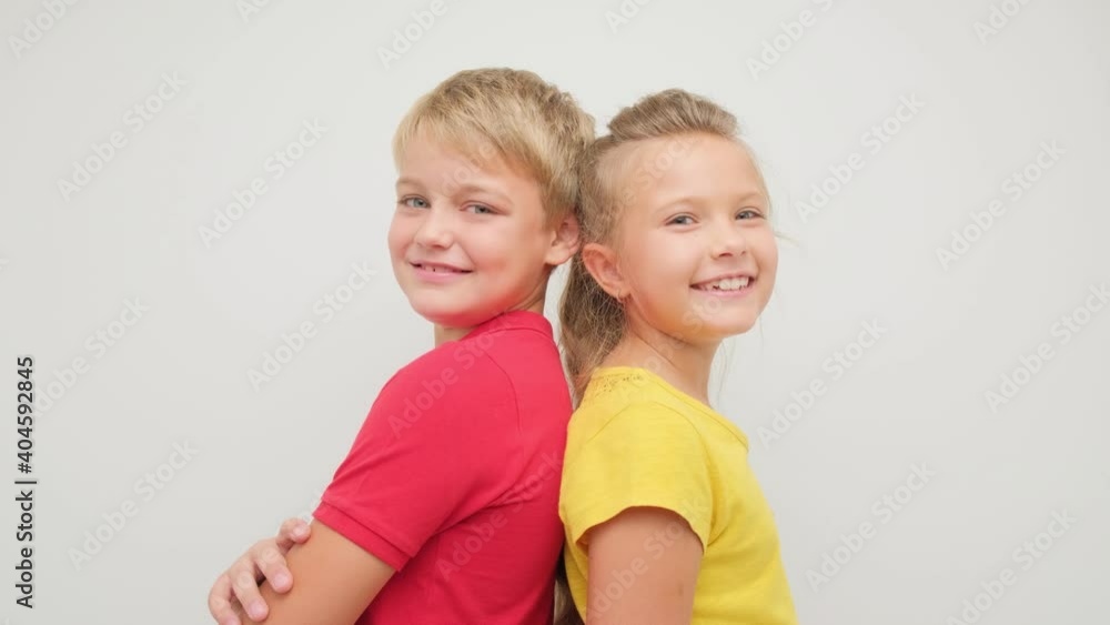 Boy and girl posing for the camera in the studio on a white background. Children turn into the camera and smile. Boy and girl posing for the camera in the studio on a white background. Children turn into the camera and smile.