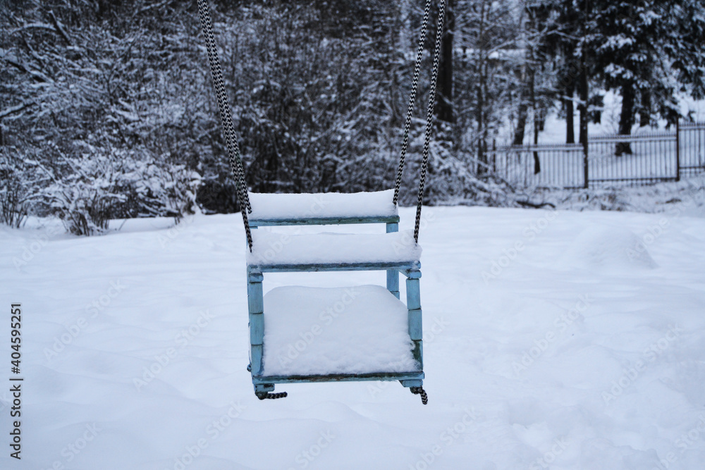 Snow covered teeter on the playground. Seat of the children's swing in winter weather, childish entertainment