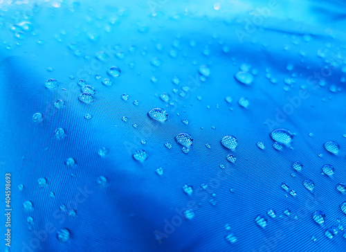 Beautiful large transparent drops of clear water after rain on blue waterproof water-repellent dense fabric used for shower curtain, umbrella, tent, waterproofing film in daylight, close-up